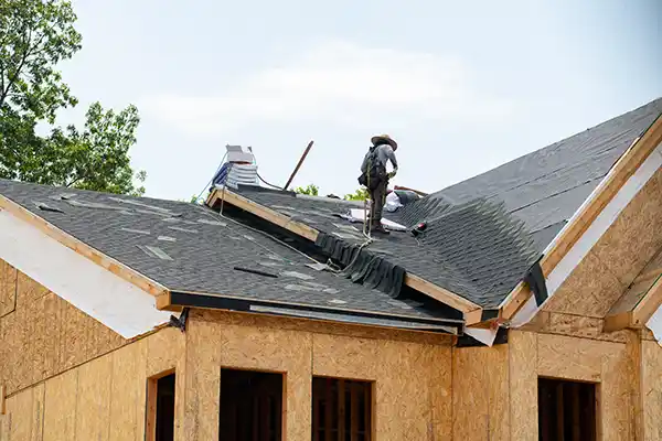 Roofers installing asphalt shingles on new home construction roof