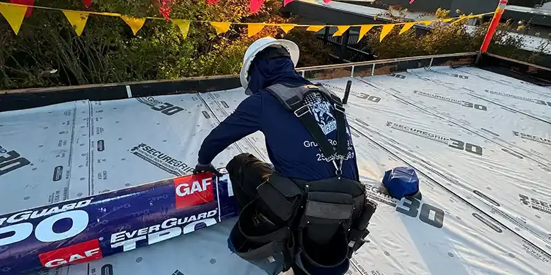 Roofing worker installing GAF EverGuard TPO membrane on flat roof
